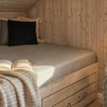 Schlafzimmer mit Holzwand, Bett, Kissen und geöffnetem Buch.
