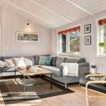 Wohnzimmer mit grauem Sofa, Holztisch und Sessel. Holzwände und Fenster mit Blick in den Wald.