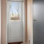 Haus mit weißen und grauen Türen, Holzwand und Fensterblick auf Bäume.