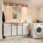 Badezimmer mit Waschmaschine, Waschbecken und Toilette. Holzwand und Fliesenboden.