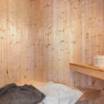 Sauna mit Holzwand, Sitzbank und Holzschale mit Besen.