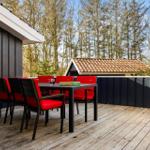 Terrasse mit Tisch und roten Stühlen, umgeben von Wald und Haus.