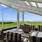 Terrasse mit Tisch und Stühlen unter weißem Dach. Blick auf Grasland und Meer.