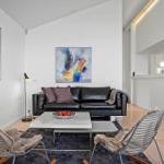 Wohnzimmer mit schwarzer Couch, zwei Stühlen und abstrakten Bildern an den Wänden.