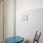 Bad mit Dusche, Toilette und blauem Sitzkissen.