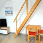 Wohnzimmer mit TV, Esstisch und Holztreppe zur oberen Etage.