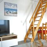 Wohnzimmer mit TV, Essbereich und Holztreppe zur oberen Etage.