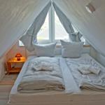 Doppelbett unter Dachschrägen mit Fenster und Nachttisch.