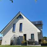 Modernes Haus mit weißen Wänden und großem Garten unter blauem Himmel.