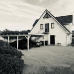 Weiße Villa mit Carport und zwei parkenden Autos.