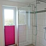 Badezimmer mit Dusche und Fenster mit rosa Jalousie.