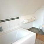 Bad mit Badewanne, Toilette und Regal an der Wand.