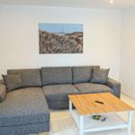 Wohnzimmer mit grauem Sofa, Holztisch und Wandbildern.