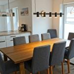 Essbereich mit Holztisch und grauen Stühlen. Küche mit Arbeitsplatte und Fenster.