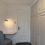 Room with desk, chair, and wardrobe. Door and wall light visible.