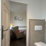 A room with chair and wall decoration. Toilet area to the right.