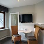 Room with TV, desk and two chairs. Window with view of roof.
