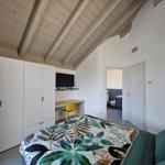 Schlafzimmer mit Bett, Kleiderschrank und Schreibtisch unter Holzdecke.