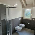 Badezimmer mit Dusche, Toilette und Waschbecken. Holzdecke und Fenster mit Blick.