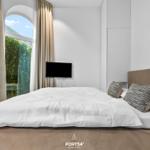 Schlafzimmer mit Bett, TV und Bogenfenster mit Blick auf Grün