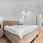 Schlafzimmer mit Bett, Nachttisch und Sessel. Holzboden und helle Wände.