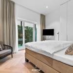 Schlafzimmer mit Bett, Sessel und Blick auf Garten.