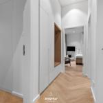 Hölzerner Boden, weiße Schränke und Blick in Schlafzimmer mit Bett und Fernseher.