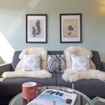 Ein grauer Sofa mit Felldecken und Kissen. Auf dem Tisch steht eine Tasse und ein Magazin.