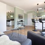 Wohnbereich mit Sofa, Couchtisch und Barhocker. Spiegelwand und Holzboden sichtbar.