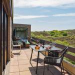 Terrasse mit Tisch, Stühlen und Blick auf grüne Hügel.