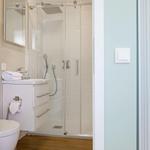 Badezimmer mit Dusche, Waschbecken und Toilette. Holzfußboden und helle Wände.