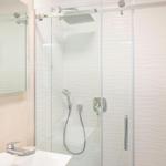 Dusche mit Glaswand, Duschbrause und Handdusche. Spiegel und Waschbecken daneben.