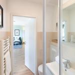 Badezimmer mit Dusche, Waschbecken und Heizkörper. Durchgang zur Wohnfläche mit Sofa.