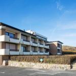 Modernes Mehrfamilienhaus mit Balkonen und Garage. Hintergrund: Hügel mit trockenem Buschwerk.