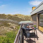 Terrasse mit Tisch und Stühlen, Blick auf Dünenlandschaft.