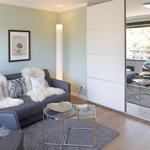 Wohnzimmer mit Sofa, Teppich und Glas-Tisch. Durchgehende Glastür führt auf Balkon.