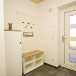 Eingangsbereich mit weißen Wänden, Holzbank und Tür mit Glasfeldern.