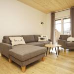 Wohnzimmer mit Sofa, Sessel und Holzboden. Fenster mit Vorhängen.