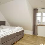 Schlafzimmer mit Doppelbett, Holzboden und Fenster mit Vorhängen.