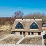 Modernes Haus mit strohgedecktem Dach und großen Fenstern in ländlicher Umgebung.