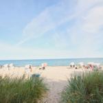 Strand mit weißen Strandkörben und Sanddünen im Vordergrund.