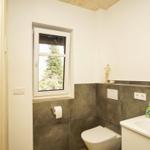 Badezimmer mit Toilette, Waschbecken und Fenster zur Waldansicht.
