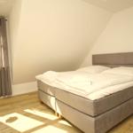 Schlafzimmer mit Doppelbett, Holzboden und Fenster mit Vorhängen.