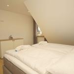 Schlafzimmer mit Doppelbett, Schrank und Fenster unter Dachschrägen.