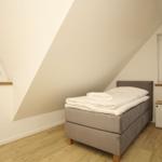 Schlafzimmer mit Dachschräge, Bett, Fenster und Holzboden.