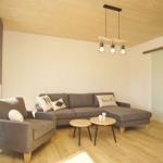 Wohnzimmer mit grauem Sofa, Holzdecke und zwei runden Tischen.
