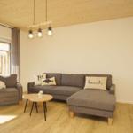 Wohnzimmer mit grauem Sofa, Tisch und Fenster. Holzdecke und Boden.