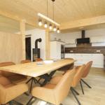 Essbereich mit Holztisch und Ledersitzen, Küche im Hintergrund, Holzdecke und -boden.