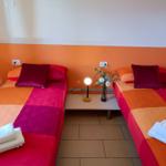 Zwei Betten mit bunten Bettwäschen und einer Tischlampe in einem Raum mit orangefarbener Wand.