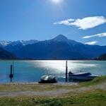 Lakeside with boats and snow-capped mountains under clear blue sky.